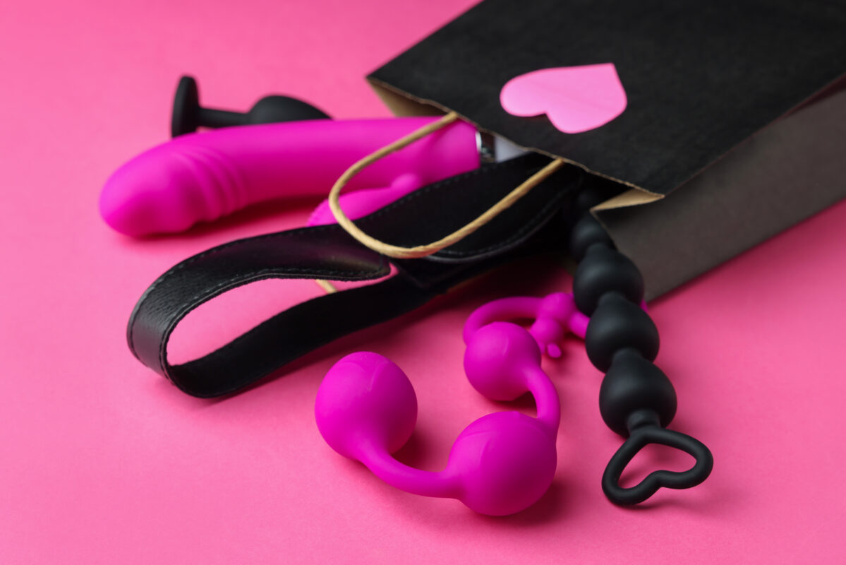 Bolsa de compras con diferentes juguetes sexuales sobre un fondo rosa, primer plano
